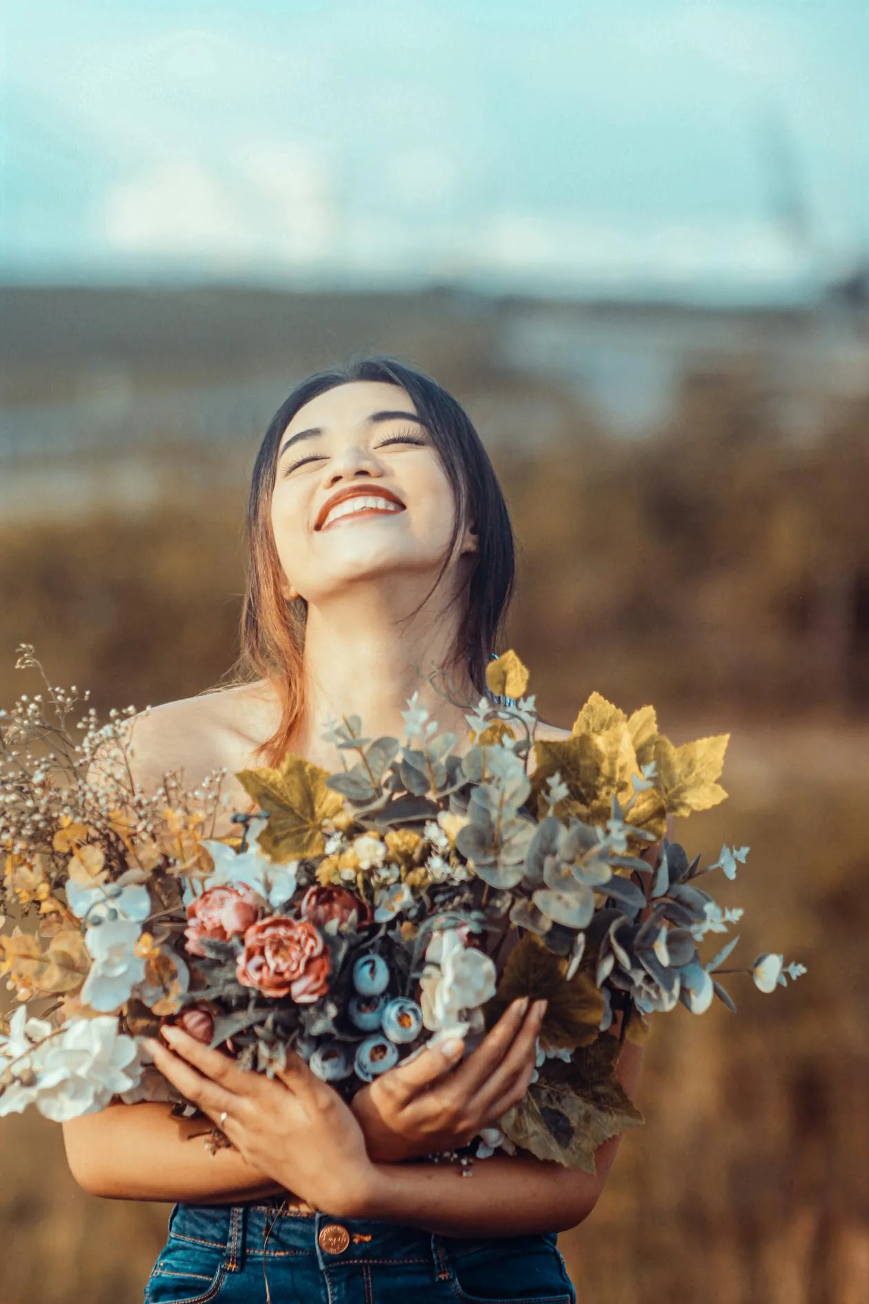 A woman holding a vibrant bouquet of flowers in an open field
