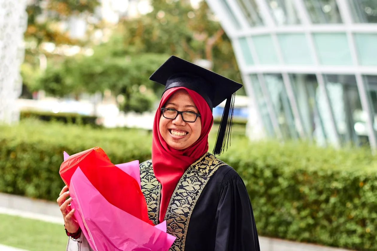 A woman in academic dress holding flowers to celebrate her achievement