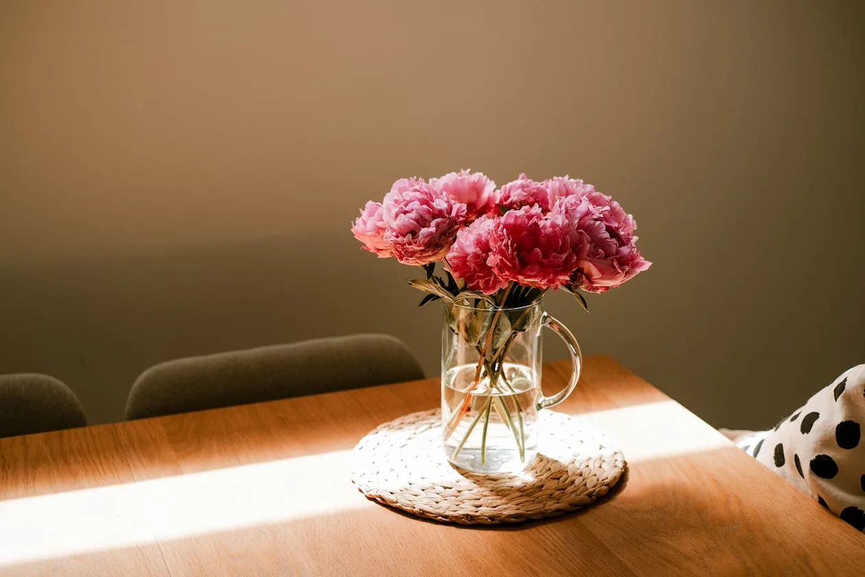 Beautiful pink peony bouquet in a glass vase on a sunlit wooden table