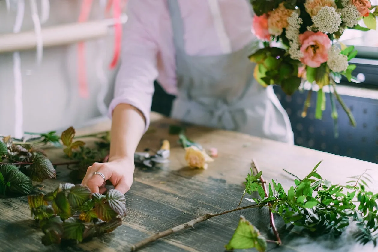 A person in an apron carefully arranging a bouquet of flowers