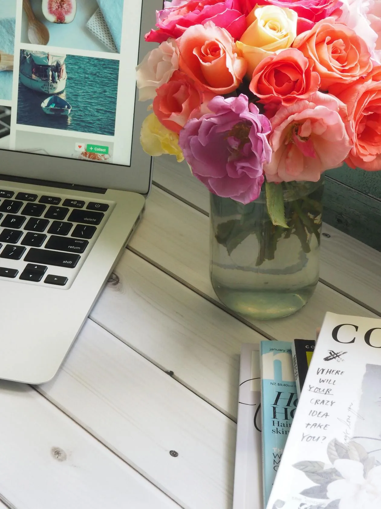 A glass vase of colourful roses on a desk beside a laptop